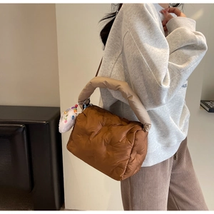 Detailed view of a brown quilted puffer shoulder bag with a plush white cloud charm accessory