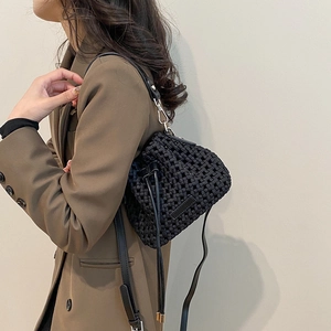 Chic black woven bucket bag with wide intrecciato leather straps worn over a vintage blazer