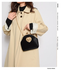 Dettaglio borsa vintage in velluto con chiusura a cuore dorata indossata con trench