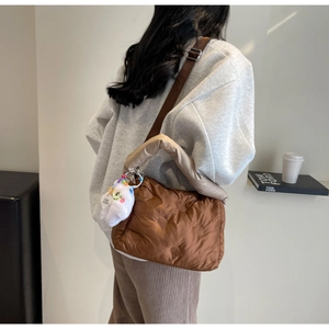Brown quilted puffer bag with plush charm and adjustable strap shown on model