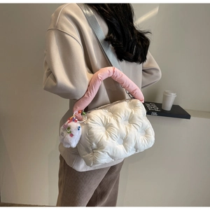 Detail of white quilted down crossbody bag with pink handle and plush charm on a model