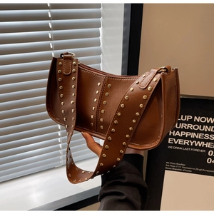 Detailed close-up of brown faux leather shoulder bag with decorative gold rivets and wide strap