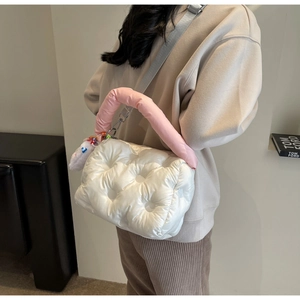 Quilted padded crossbody bag with pink handle and cute plush charm on a female model