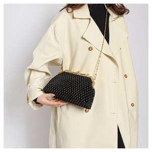 Detail of black suede shell bag with golden metal dots and chain strap worn on beige coat