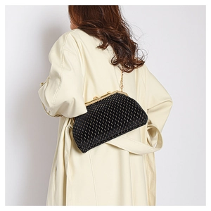 Detail of elegant black velvet shell bag with gold chain strap on a beige trench coat