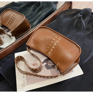 Detail view of brown vintage underarm bag with gold rivets on black silk background