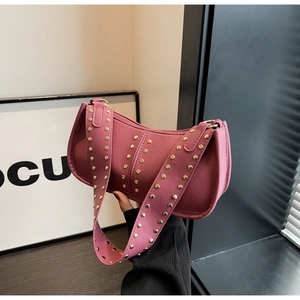 Detail of dark pink leather crescent bag featuring golden rivets and a wide shoulder strap