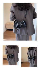 Detail of black motorcycle style underarm bag with gold rivets and wide shoulder strap