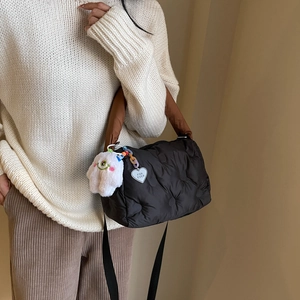 Quilted puffer tote bag in black nylon with brown handles and a plush monster charm