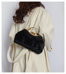 Detail of black velvet clutch with bamboo patterns shown on a model in beige coat