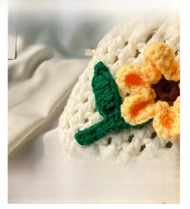 Close-up of white crochet bucket bag featuring green leaf and sunflower knitted charms