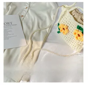 Detail view of pearl chain strap on a white crochet bucket bag with yellow floral decor