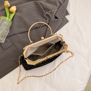 Retro black shell evening bag with gold textured dots and metal circular handle on white bedding