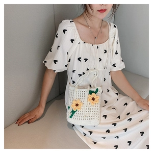 Detail of hand-knitted white bucket bag with floral daisy decor and pearl shoulder strap