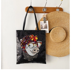 Detail of black sequin tote bag with a whimsical pig illustration on a wooden hanger