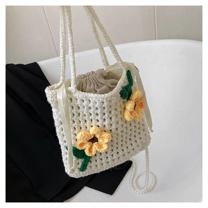 Detail of hand-woven white bucket bag featuring yellow crochet flowers and pearl strap