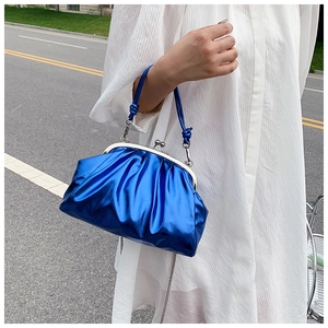 Gros plan d'un sac à plis bleu métallisé avec poignée et chaîne sur robe blanche