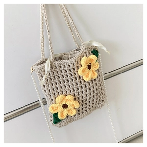 Detail of hand-woven beige bucket bag featuring yellow flowers and a pearl chain strap