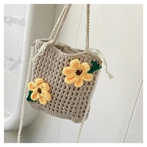 Detail of hand-woven beige bucket bag with yellow sunflower motifs and pearl chain