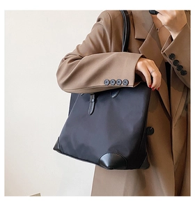 Detail of black nylon tote bag with leather handles shown on shoulder with blazer