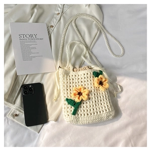 Close-up of a handmade knit bucket bag with pearl strap and yellow sunflower accents