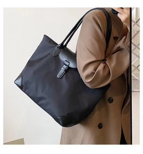 Detail showing high-capacity black tote bag with leather trim on model in brown suit