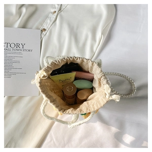 Detail of beige knit bucket bag with pearl strap and internal space for cosmetics