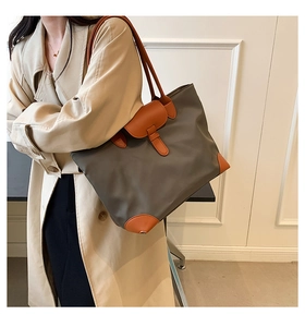 Fashionable grey nylon tote bag with brown leather accents worn by a model in a modern style