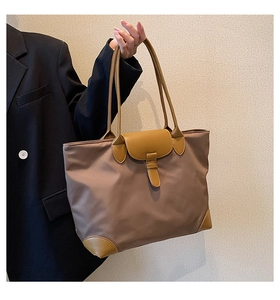 Detail of a large brown nylon tote bag with yellow leather handles held by a model