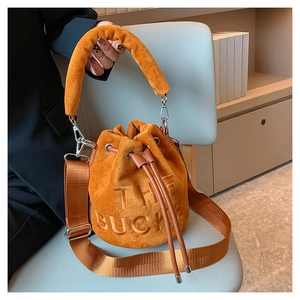 Detail of bright orange velvet bucket bag featuring The Bucket embroidery and plush handle