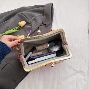 Chinese style embroidered clutch bag with golden metal frame shown with daily essentials