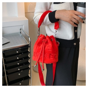 Red plush drawstring bucket bag with embossed The Bucket text and wide shoulder strap