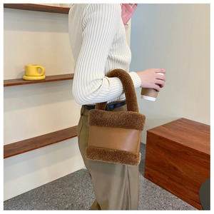 Détail du sac seau en peluche marron et cuir porté par un mannequin en extérieur