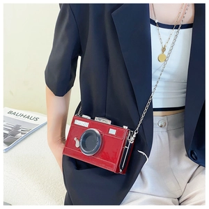 Detail of red patent leather camera-shaped crossbody bag with silver chain strap on model