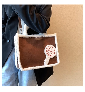 Detail of suede tote bag featuring fuzzy white shearling trim and floral plush patch