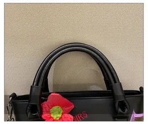Close-up of black leather bucket bag handle with red crochet flower and HRS embroidery