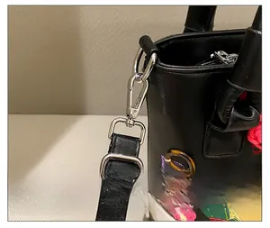 Detail of silver hardware D-ring and colorful floral embroidery on black leather bag