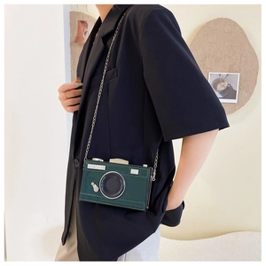 Detail of a dark green vintage camera-shaped crossbody bag with a silver chain strap