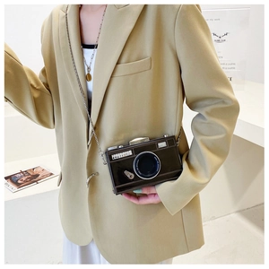 Detail of camera-shaped crossbody bag with metallic lens and chain strap on model
