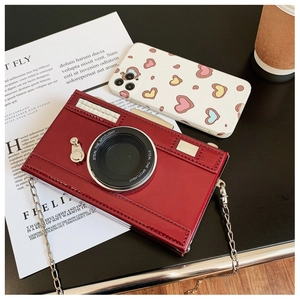 Detail shot of a burgundy camera-shaped crossbody bag with glossy finish and chain strap