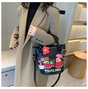 Detail of a black bucket bag with colorful Thai embroidery and floral charms in a cozy room