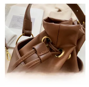 Detail of a brown leather drawstring bag with metallic eyelets and adjustable strap