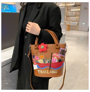 Brown bucket bag featuring Thai-style colorful embroidery worn by a model in a black suit
