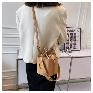 Chic light brown drawstring bucket bag with gold hardware shown as a crossbody