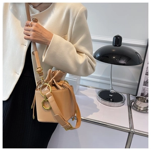 Detail view of a beige drawstring bucket bag with gold geometric charm and long strap