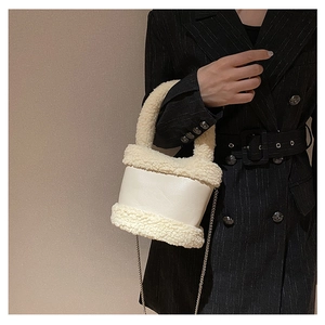 Detail of cream plush bucket bag with leather patchwork and metal chain strap on model