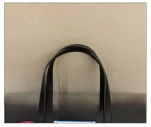Detail of comfortable flat handle and leather texture on a black embroidered tote bag