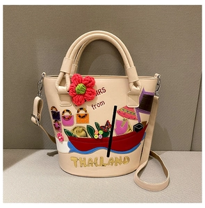 Detail of cream bucket bag featuring Thai embroidery and long shoulder strap