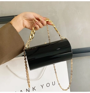 Détail d'un sac cylindrique noir brillant avec poignées décoratives en chaîne dorée