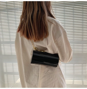 Détail d'un sac cylindre noir brillant avec une grosse chaîne dorée sur un mannequin